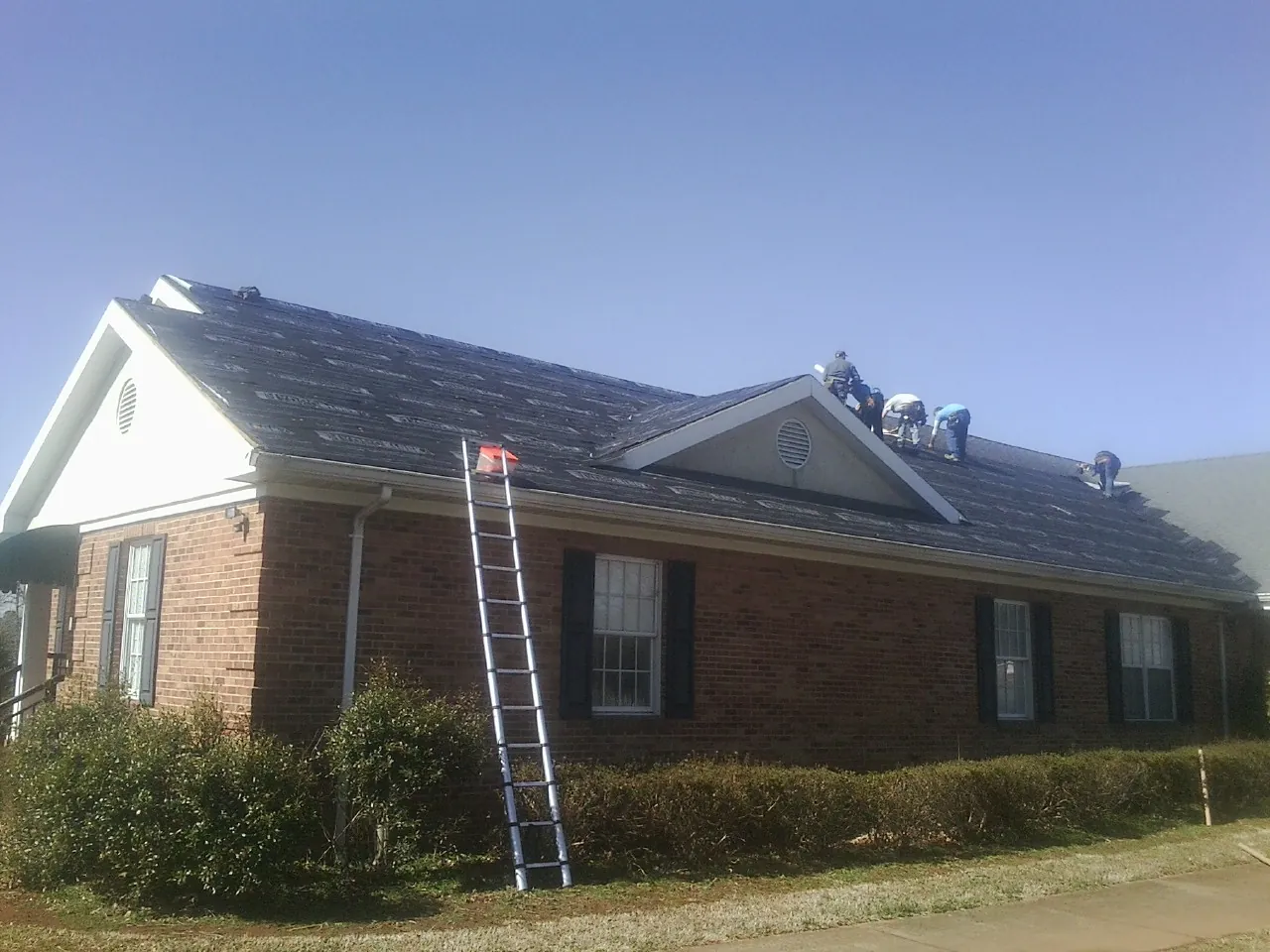 Crew tearing shingles off a brick ranch roof with a ladder set — Metal Roof Repair work by our crew in New York Mills