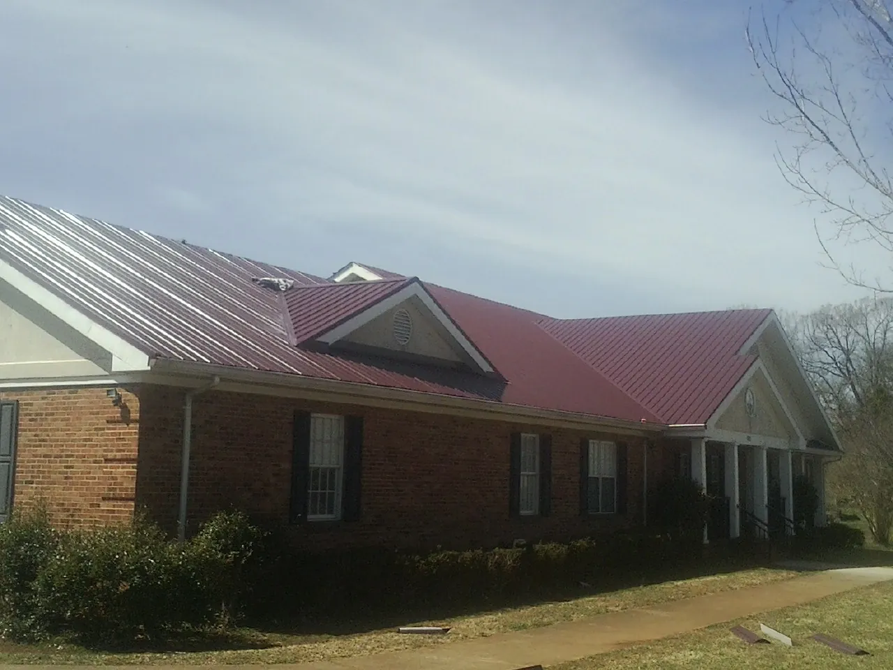 Red metal roof with gabled entries on a long brick building, from a Hail Damage Roof Repair job in New York Mills