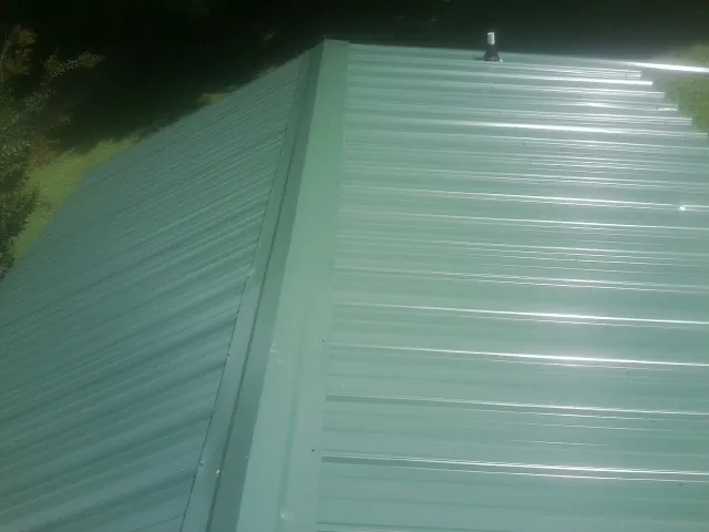 New green metal panels meeting at the ridge of a roof — Flat Roof Repair work by our crew in New York Mills