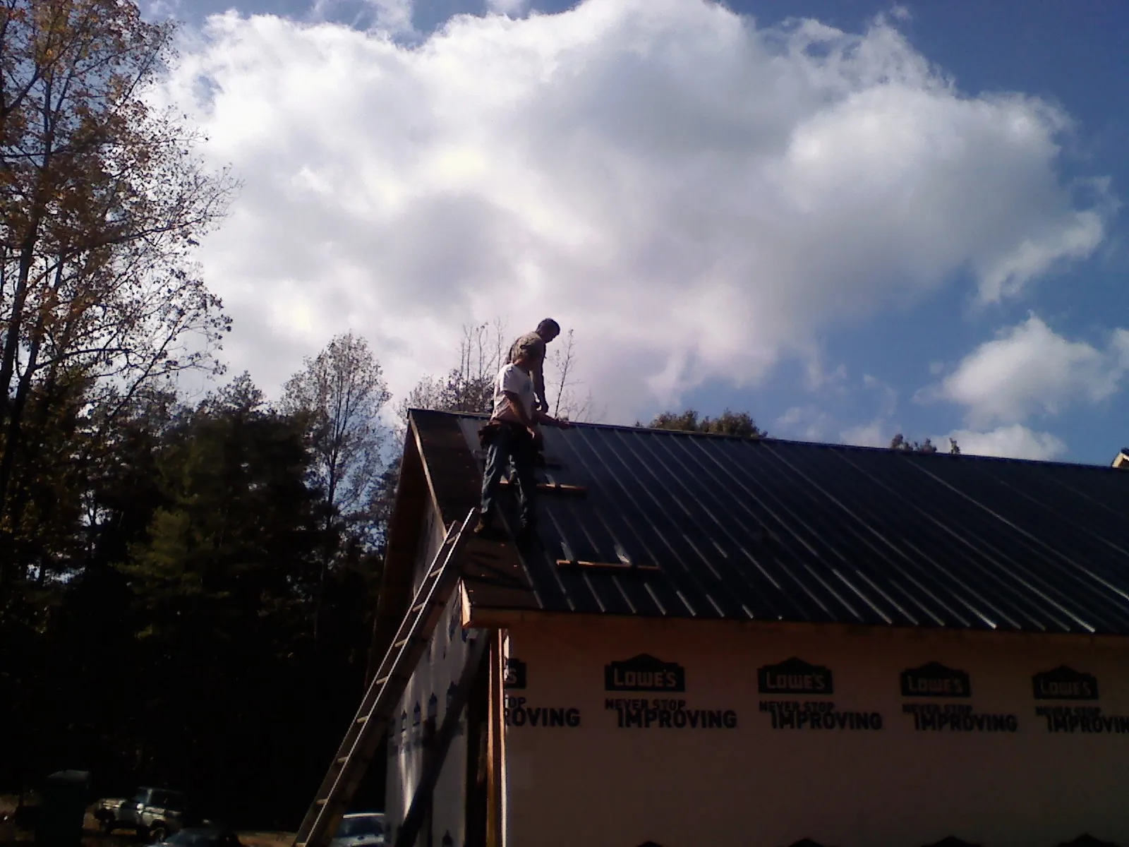 Roofer fastening dark metal panels high against a cloudy sky, from a Roof Inspection job in New York Mills