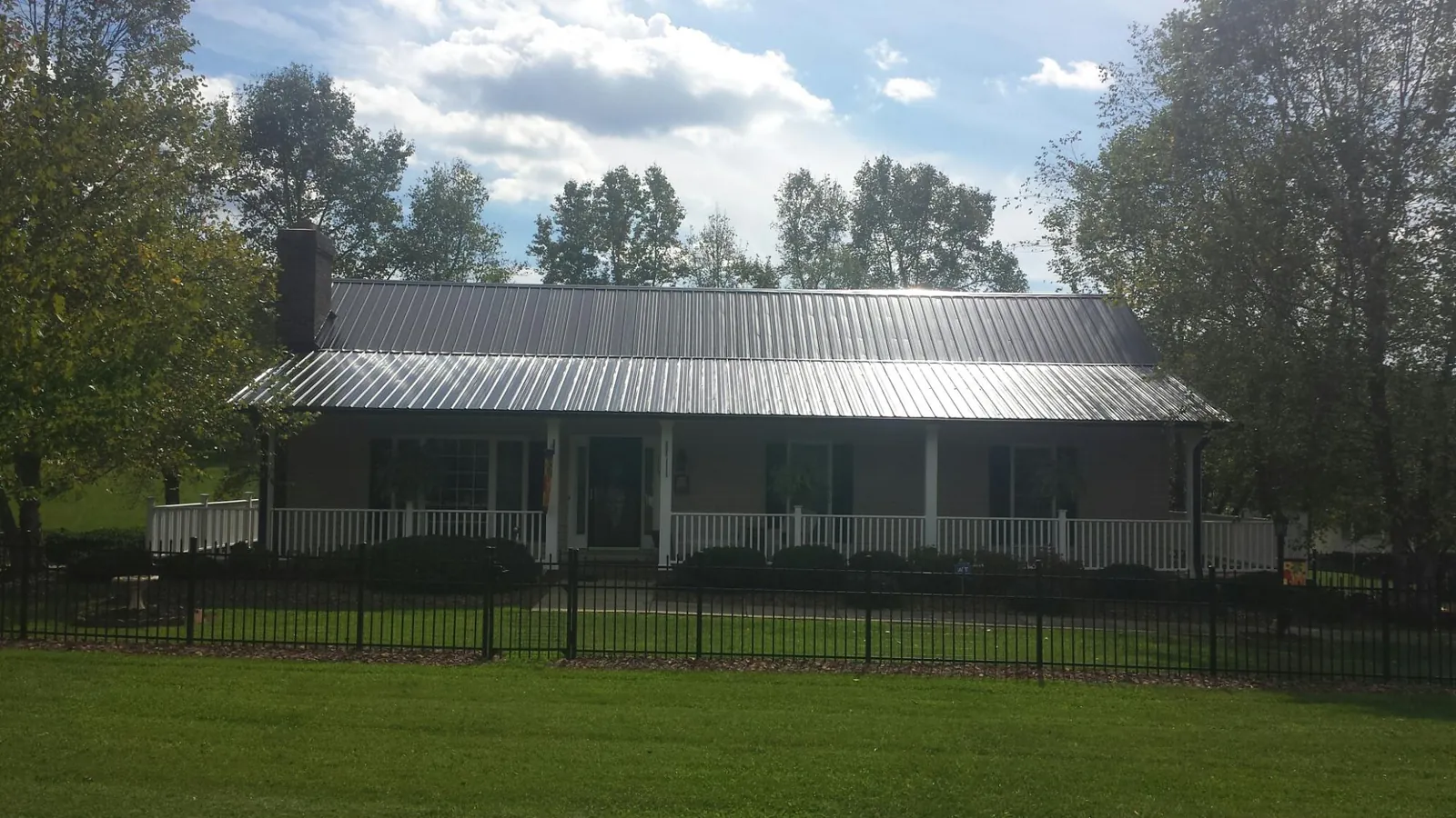 Gray metal roof on a brick ranch with a full width front porch — Gutter Guard Installation work by our crew in New York Mills