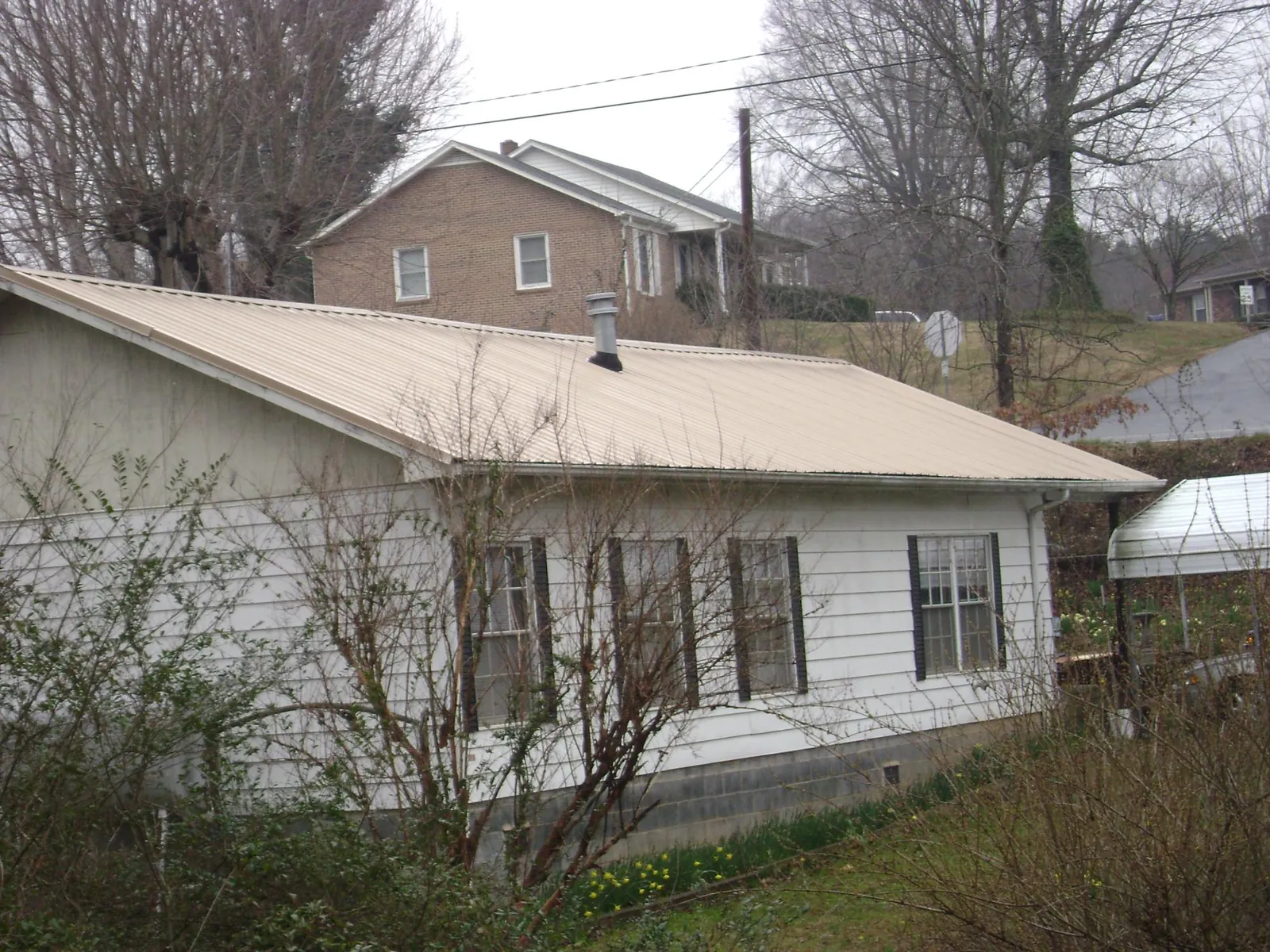 Tan metal roof on a white sided house set into a hillside — Commercial Roofing by Roofing Brothers in New York Mills